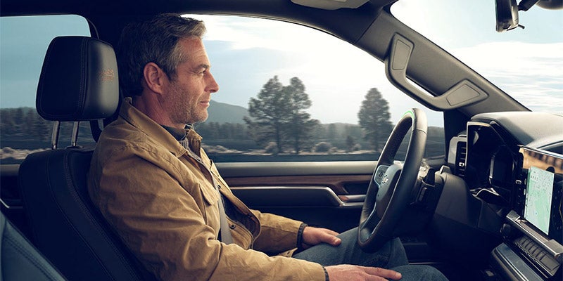 A man seated in the driver's seat of a Chevrolet Silverado 1500, focused on the road ahead, with a determined expression.